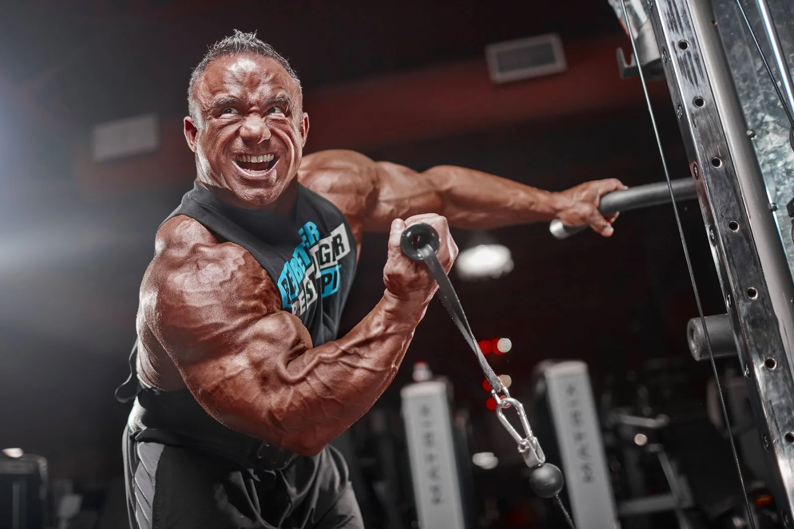 Bodybuilder working an arm on a cable machine, side lit