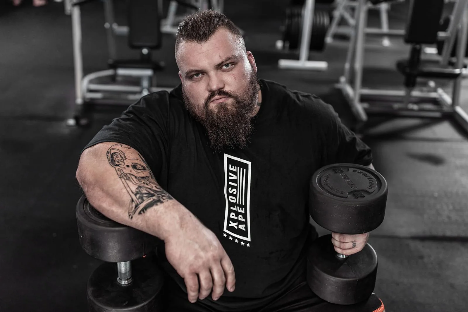 Big bearded man seated with forearms on his knees in a gym