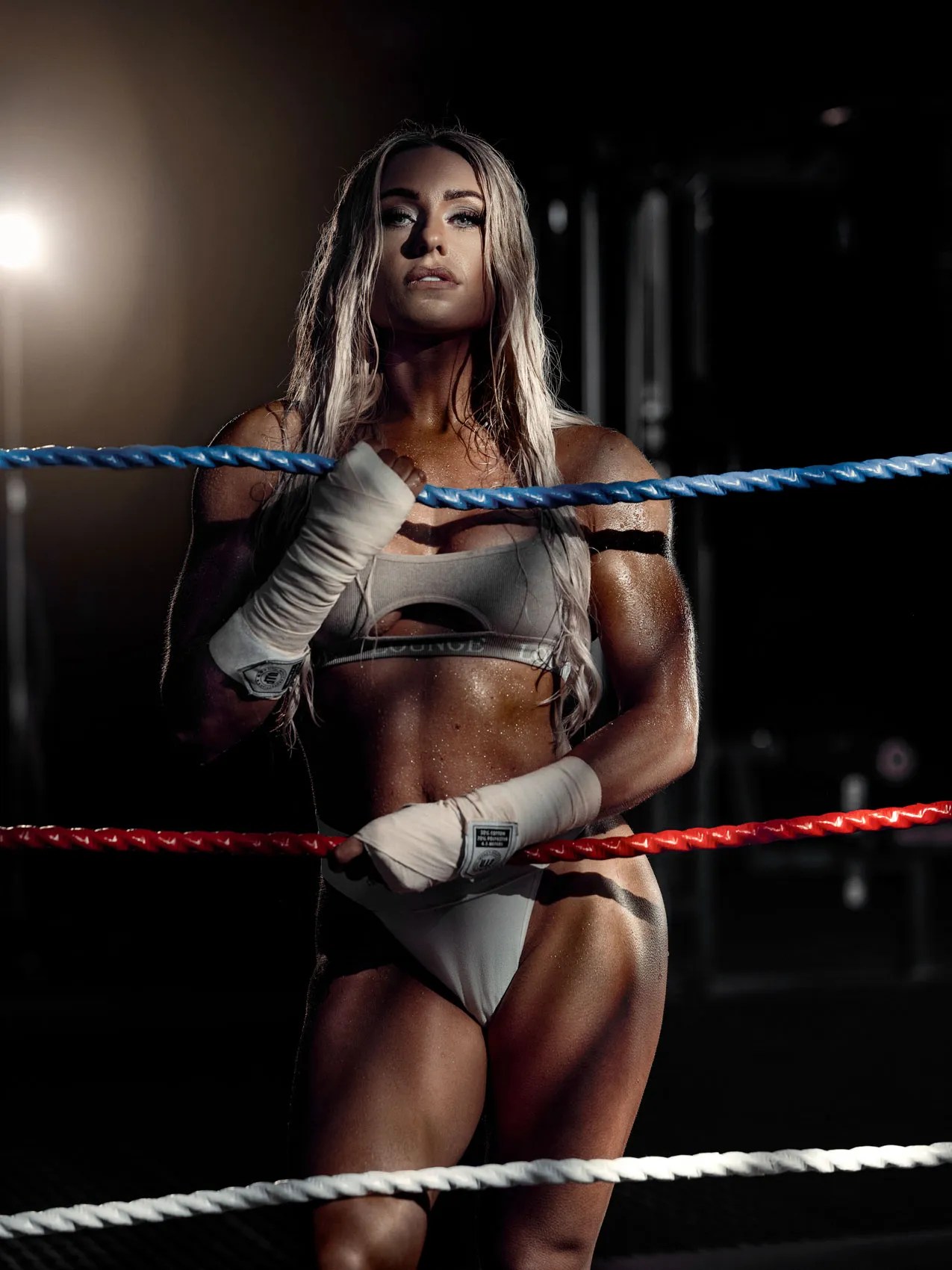 Female athlete in hand wraps standing in a boxing ring under a single light