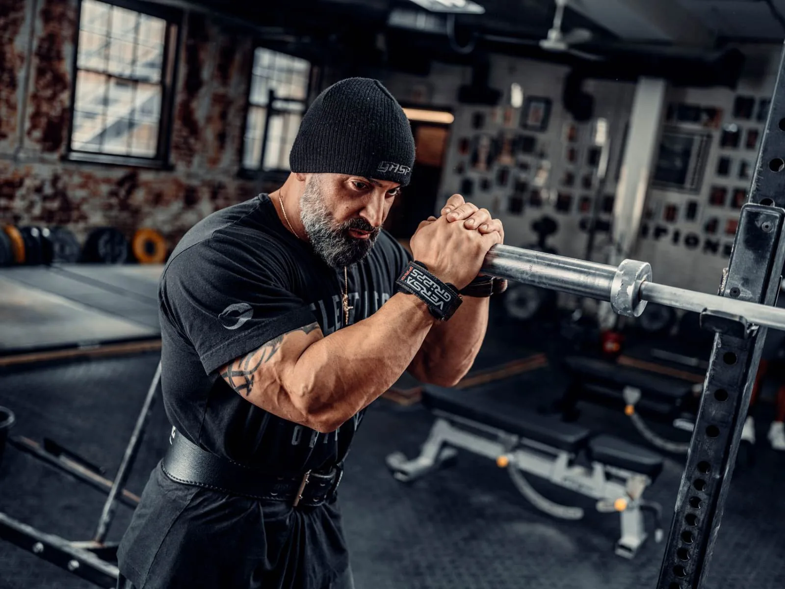 Man in a beanie and lifting straps gripping a cable bar in the gym