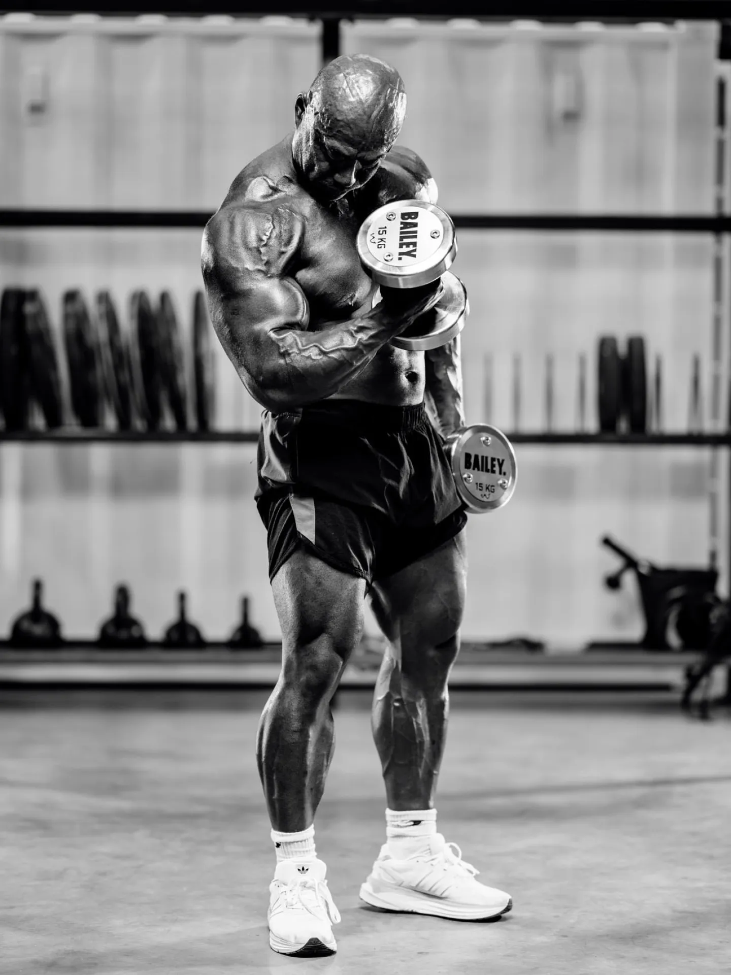 Black and white photograph of a bodybuilder curling a dumbbell in the gym