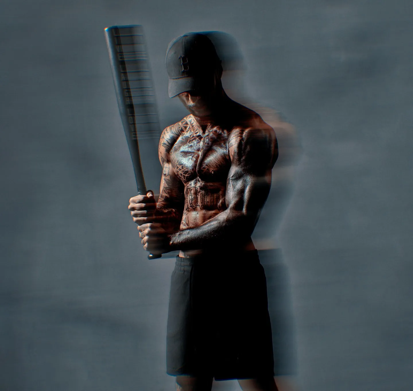 A heavily tattooed muscular man holding a baseball bat, shirtless and wearing a cap, photographed against a grey background with a motion blur effect